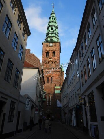 Tour de l'église dans une ruelle étroite à Copenhague, Danemark, avec un ciel partiellement nuageux et des bâtiments historiques de chaque côté.