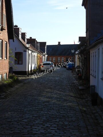 Rue pavée à Ribe, Danemark, avec des maisons colorées et des voitures stationnées.