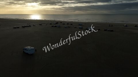 Vue aérienne d'un groupe de camping-cars sur la plage de Romo, au Danemark, avec l'océan en arrière-plan et un ciel nuageux.