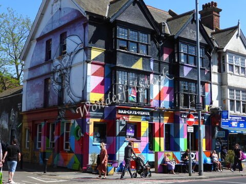 Bâtiment coloré avec un mur peint, situé à Brighton, Angleterre, où des personnes se déplacent et s'asseyent sur une terrasse.