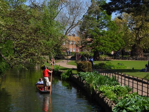 Un bateau navigue sur un canal à Canterbury, Angleterre, entouré de verdure et de personnes se reposant dans le parc.