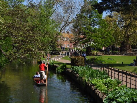 Un bateau navigue sur un canal à Canterbury, Angleterre, entouré de verdure et de personnes se reposant dans le parc.