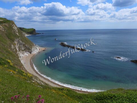Plage de Durdle Door en Angleterre, avec des falaises et des eaux calmes sous un ciel nuageux.