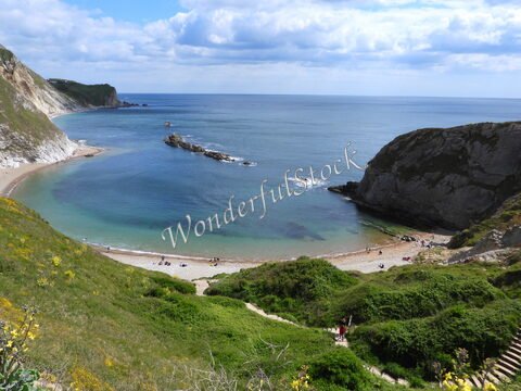 Plage de Durdle Door en Angleterre, avec des falaises verdoyantes et une mer calme.