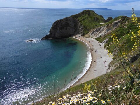 Plage de Durdle Door en Angleterre, avec des falaises et des baigneurs sur le sable.