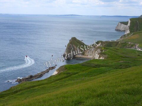 Durdle Door en Angleterre, avec des falaises blanches surplombant la mer et un bateau à moteur naviguant près de la côte.