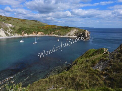 Plage de Durdle Door en Angleterre, avec des voiliers et des falaises verdoyantes sous un ciel nuageux.