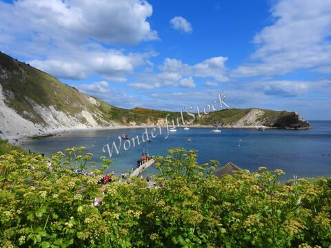 Plage entourée de falaises à Durdle Door, Angleterre, avec des bateaux au mouillage et des visiteurs sur le chemin.