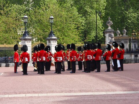 Musiciens en uniformes rouges à Londres, Angleterre, avec des chapeaux en fourrure, près d'une grille ornée.