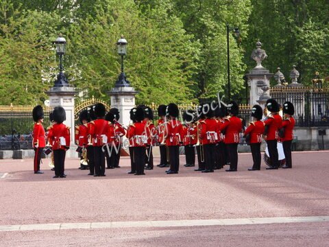 Musiciens en uniformes rouges à Londres, Angleterre, avec des chapeaux en fourrure, près d'une grille ornée.