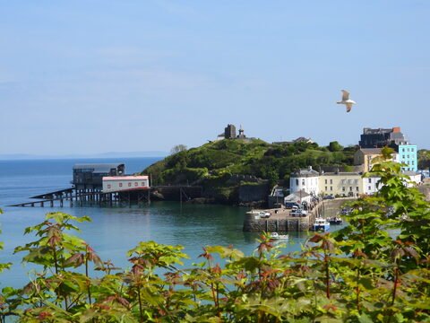 Bâtiments colorés et quai à Tenby, pays de Galles, avec une mer calme et une colline verdoyante en arrière-plan.