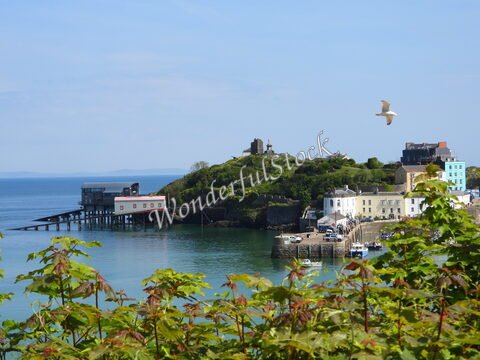 Bâtiments colorés et quai à Tenby, pays de Galles, avec une mer calme et une colline verdoyante en arrière-plan.