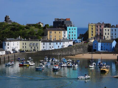 Bateaux de pêche au port de Tenby, pays de Galles, avec des maisons colorées en arrière-plan et une plage de sable.