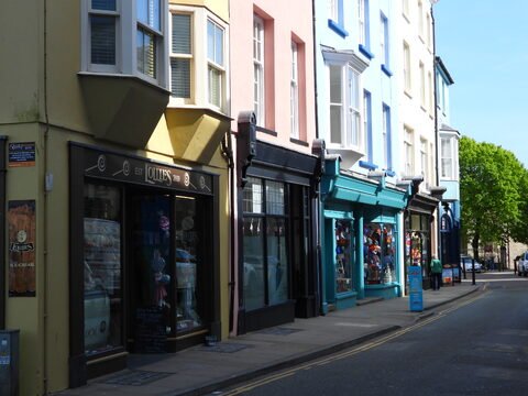 Boutiques colorées sur une rue de Tenby, pays de Galles, avec des arbres verdoyants et des enseignes commerciales visibles.