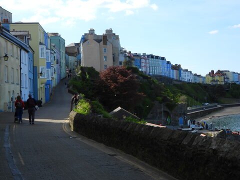 Maisons colorées sur une rue à Tenby, pays de Galles, avec des collines verdoyantes en arrière-plan et une vue sur la mer.