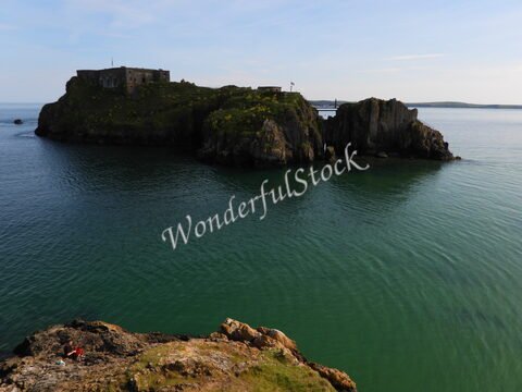Un rocher avec des ruines surplombant l'eau calme à Tenby, pays de Galles.