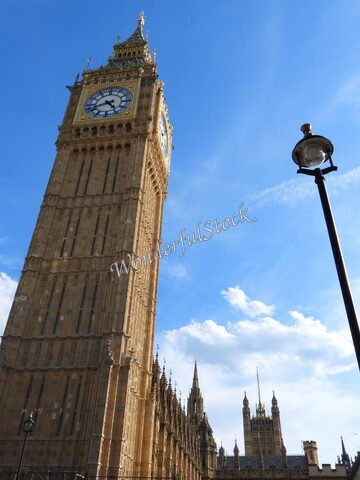 Big Ben à Londres, Angleterre, avec un lampadaire en premier plan et un ciel bleu parsemé de nuages.
