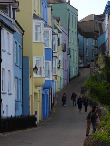 Des maisons colorées sur une rue à Tenby, pays de Galles, avec des passants et une pente menant à des bâtiments en arrière-plan.