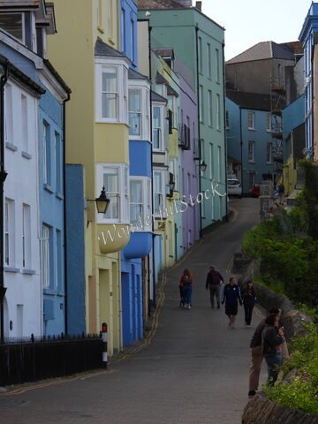Des maisons colorées sur une rue à Tenby, pays de Galles, avec des passants et une pente menant à des bâtiments en arrière-plan.