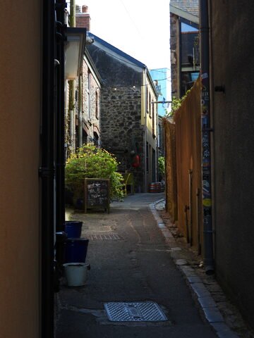 Rue étroite avec des maisons en pierre et des pots de fleurs à Tenby, pays de Galles. Un tableau noir indique un café à proximité.