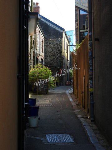 Rue étroite avec des maisons en pierre et des pots de fleurs à Tenby, pays de Galles. Un tableau noir indique un café à proximité.