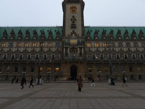 Hôtel de ville à Hambourg, Allemagne, avec une façade ornée et une horloge, entouré de passants sur une place pavée.