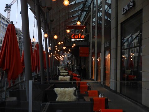 Terrasse d'un café avec des parasols rouges à Hambourg, Allemagne, éclairée par des lampes suspendues et entourée de boutiques.