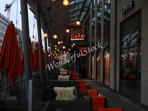 Terrasse d'un café avec des parasols rouges à Hambourg, Allemagne, éclairée par des lampes suspendues et entourée de boutiques.