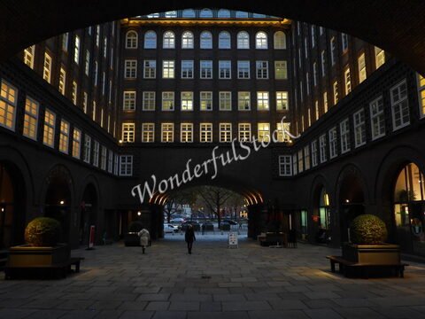 Un passage avec des arches et des fenêtres illuminées à Hambourg, Allemagne, entouré de bancs et de plantes.