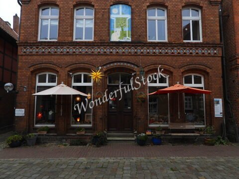 Façade en briques d'un bâtiment avec parasols blancs et orange à Hitzacker, Allemagne, ornée d'une étoile lumineuse et de pots de fleurs.