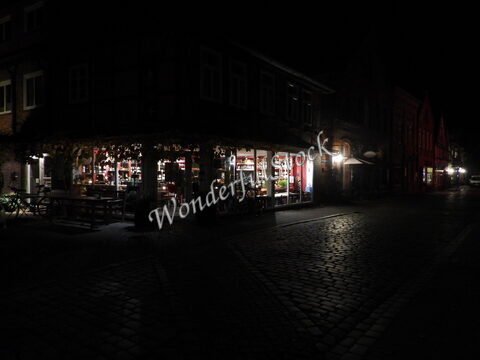 Boutique éclairée dans une rue pavée à Hitzacker, Allemagne, avec des bâtiments en briques et une ambiance nocturne.