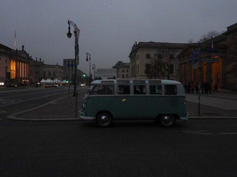 Un véhicule vintage stationné sur une rue à Berlin, Allemagne, avec des bâtiments historiques en arrière-plan et un ciel sombre.