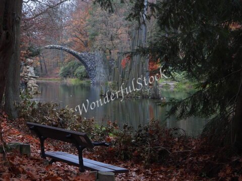 Un banc en bois près d'un étang avec le pont des Diables en Allemagne, entouré d'arbres aux feuilles d'automne.