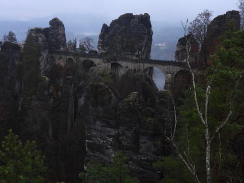 Pont de Bastei, Allemagne, entouré de formations rocheuses et de forêts, sous un ciel nuageux.