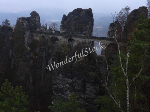 Pont de Bastei, Allemagne, entouré de formations rocheuses et de forêts, sous un ciel nuageux.