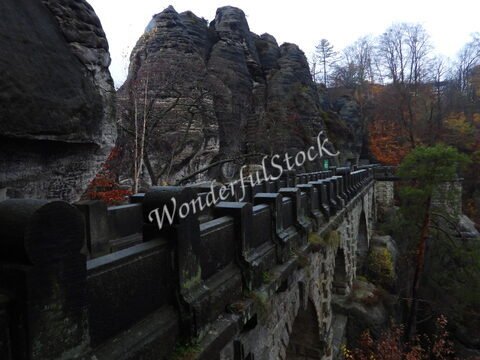 Pont en pierre surplombant des formations rocheuses à Bastei, Allemagne, entouré d'arbres aux couleurs automnales.