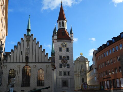 Une tour avec un toit pointu et des sculptures, située à Munich, Allemagne, entourée de bâtiments historiques et d'un ciel bleu.