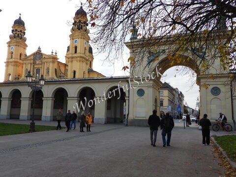 Église et arc de triomphe à Munich, Allemagne, avec des passants et des lampadaires dans un cadre urbain.