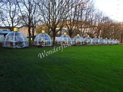 Des igloos transparents dans un parc à Baden-Baden, Allemagne, entourés d'arbres et d'herbe verte.
