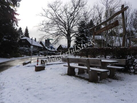 Bancs en bois recouverts de neige à Bad Wildbad, Allemagne, avec une signalisation pour la montagne et des maisons en arrière-plan.