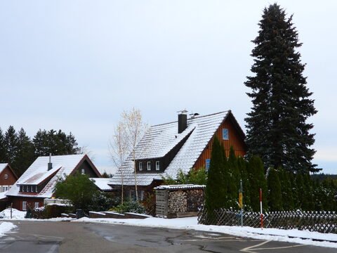 Maisons avec toits enneigés à Bad Wildbad, Allemagne, entourées de conifères et d'une route légèrement mouillée.