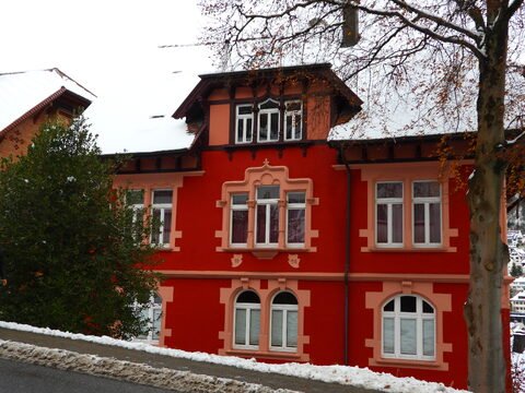 Maison colorée avec des fenêtres blanches à Triberg, Allemagne, entourée de neige et de verdure.