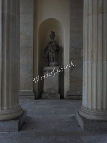 Statue entre des colonnes, Berlin, Allemagne, avec un éclairage tamisé et des murs en pierre.