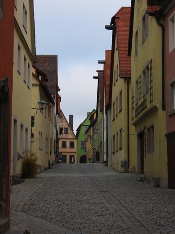 Rue pavée à Rothenburg, Allemagne, bordée de maisons aux façades colorées et aux toits en tuiles, sous un ciel nuageux.
