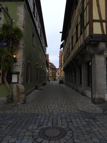 Ruelle pavée à Rothenburg, Allemagne, bordée de maisons à colombages et de murs en pierre, sous un ciel gris.