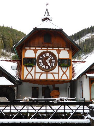 Horloge en bois ornée, à Triberg, Allemagne, avec un toit enneigé et des fleurs sur les rebords des fenêtres.