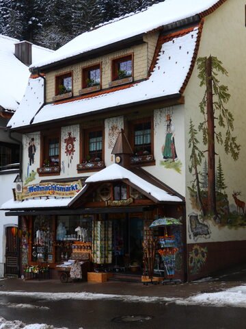 Boutique décorée avec des peintures murales, située à Triberg, en Allemagne, sous la neige, avec des articles de Noël en exposition.