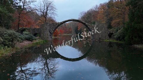 Pont en pierre se reflétant dans l'eau, entouré d'arbres aux feuilles d'automne, à la silhouette du Pont des Diables en Allemagne.