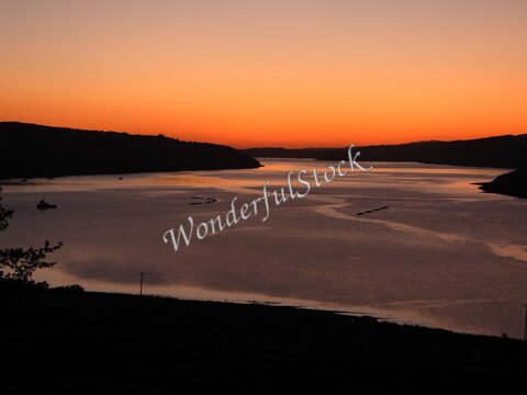 Coucher de soleil sur un cours d'eau en Écosse, avec des silhouettes de collines à l'horizon et un reflet doré sur l'eau.