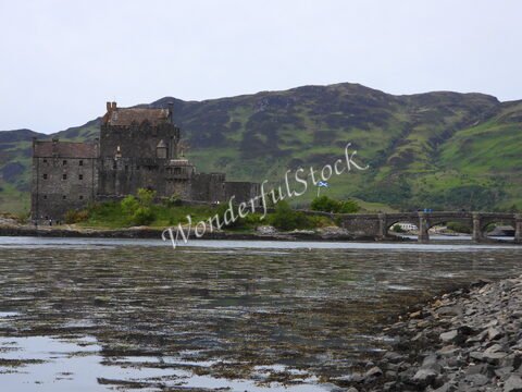 Château Eilean Donan en Écosse, avec des montagnes en arrière-plan et un pont en pierre traversant une étendue d'eau.